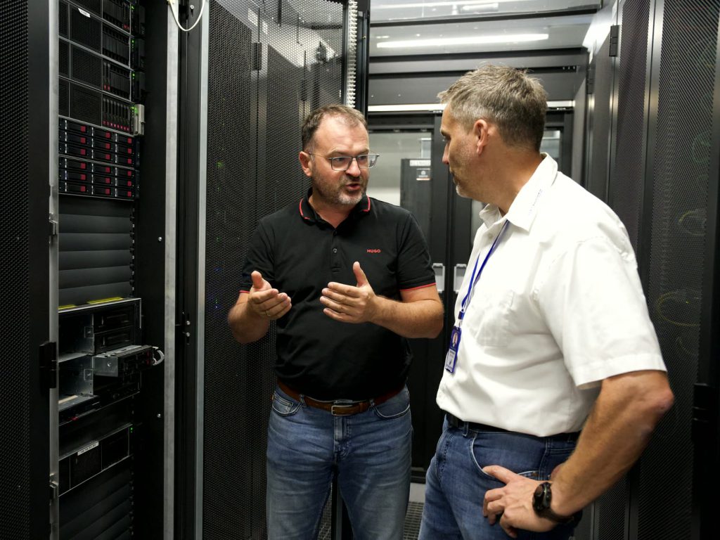 Wolfgang Asbeck erklärt im Gang zwischen den Serverschränken etwas, Bernhard Schlögl hört zu.